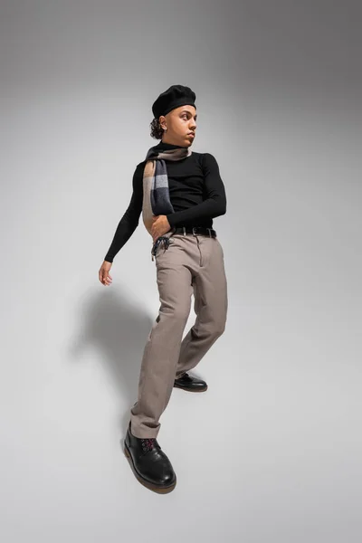Trendy african american guy in black beret and sweater with scarf looking away on grey background — Stock Photo