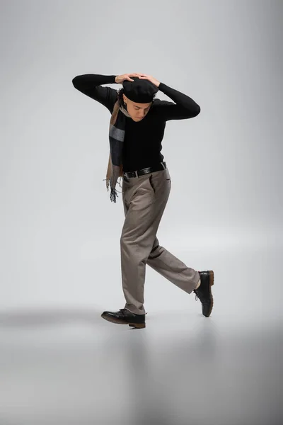 Pleine longueur de l'homme afro-américain en béret noir et pull avec foulard à carreaux marchant avec les mains au-dessus de la tête sur fond gris — Photo de stock