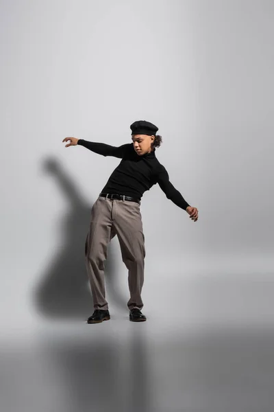 Full length of young and stylish african american guy in black beret and turtleneck with pants posing on grey background — Stock Photo