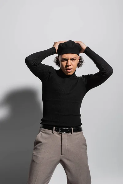 Frowning african american man in black pullover and stylish beret posing with hands on head on grey background — Fotografia de Stock