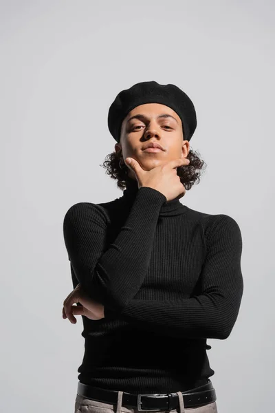Fashionable african american guy in black beret and turtleneck posing with hand near chin isolated on grey — Fotografia de Stock