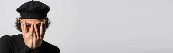 Young african american man in black beret covering face with hands isolated on grey with copy space, banner — Stock Photo