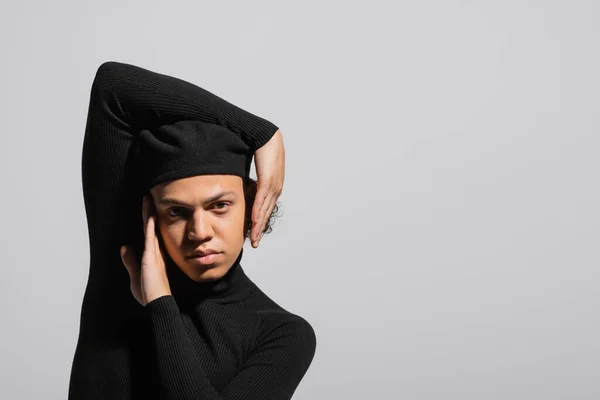 Portrait of trendy african american man in black beret and pullover posing with hands near face isolated on grey — Stock Photo