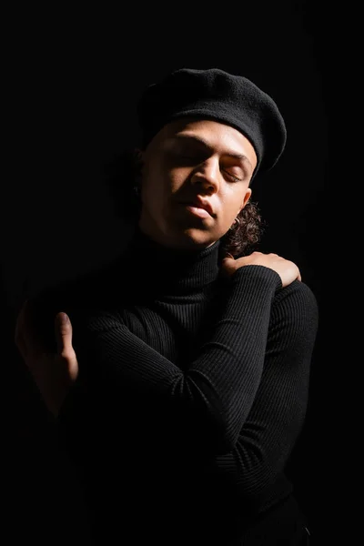 Young and trendy african american man in beret and sweater posing with closed eyes isolated on black — Stock Photo