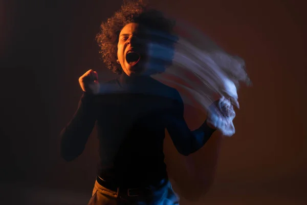 Motion blur of african american man with bipolar disorder and injured face screaming with closed eyes on dark background with orange and blue light — Stockfoto