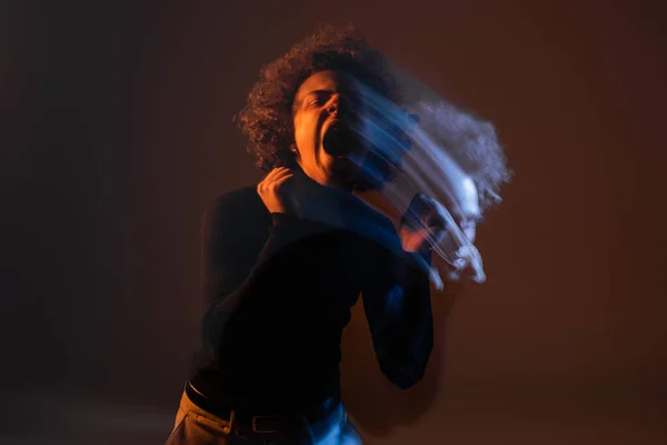 Dupla exposição de homem americano africano irritado com transtorno bipolar gritando em fundo escuro com luz laranja e azul — Fotografia de Stock