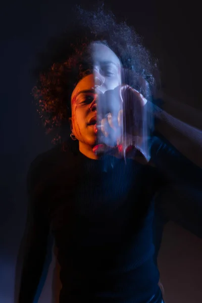 Larga exposición del hombre afroamericano lesionado con trastorno bipolar en negro con luz naranja y azul - foto de stock
