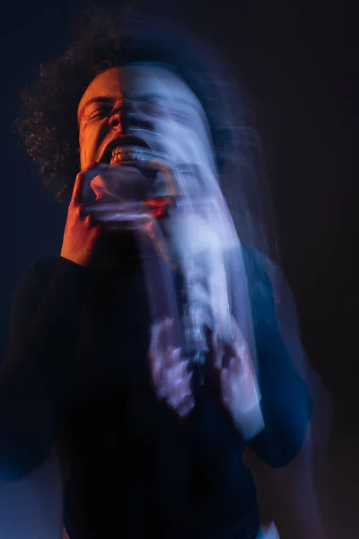 Larga exposición del hombre afroamericano herido con trastorno bipolar y mueca enojada en negro con luz naranja y azul - foto de stock
