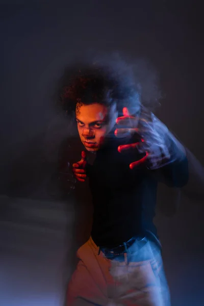 Doble exposición del hombre afroamericano lesionado con trastorno bipolar y manos ensangrentadas gestos en la oscuridad con luz naranja y azul - foto de stock