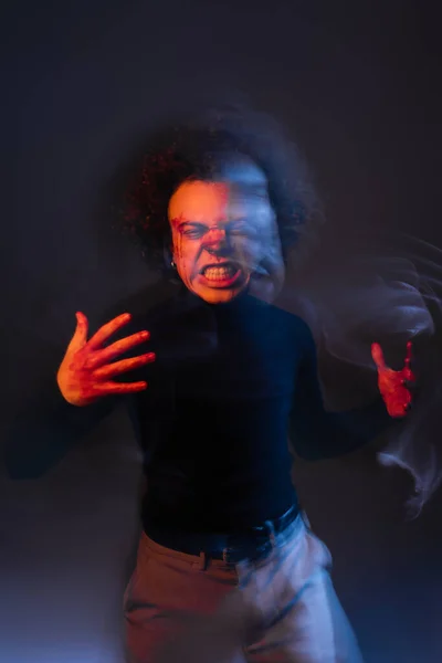 Doble exposición de hombre afroamericano enojado con la cara lesionada y trastorno bipolar mueca en la oscuridad con luz naranja y azul - foto de stock