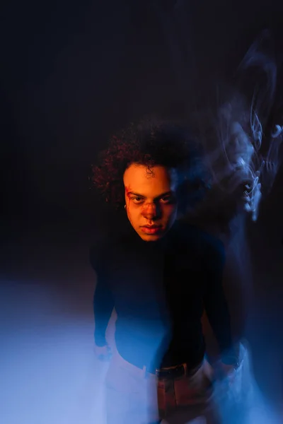 Homem afro-americano ferido com transtorno bipolar e rosto sangrento olhando para a câmera no fundo escuro com luz laranja e azul — Fotografia de Stock