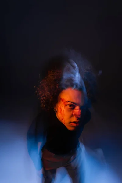 Double exposure of african american man with bipolar disorder and bleeding face looking at camera on black with orange and blue light — Stock Photo