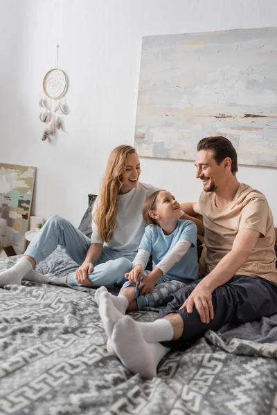 Happy parents looking at daughter smiling while sitting on bed — Photo de stock