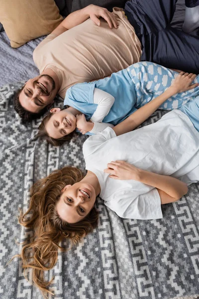 Top view of happy parents and cheerful kid lying on bed — Stock Photo