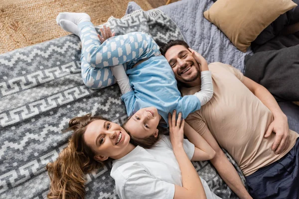 Top view of positive parents and cheerful kid lying on bed at home - foto de stock