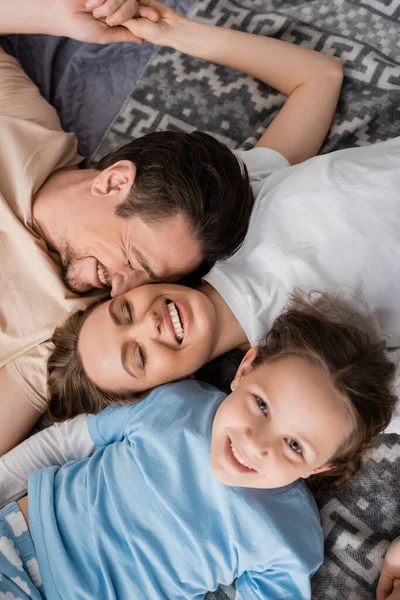 Top view of joyful parents with closed eyes and happy kid lying on bed at home — Stock Photo