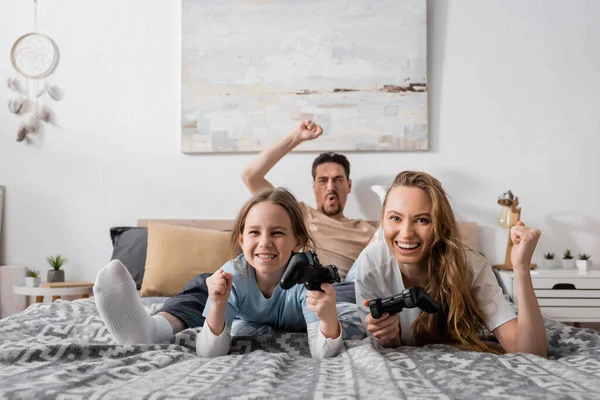 KYIV, UKRAINE - NOVEMBER 28, 2022: excited woman and kid holding joysticks near blurred husband on background — Stock Photo