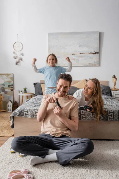 KYIV, UKRAINE - NOVEMBER 28, 2022: happy parents playing video game near excited daughter in bedroom — Stock Photo