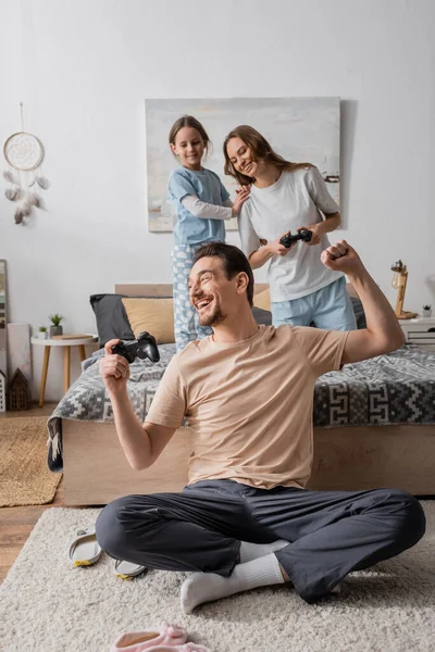 KYIV, UKRAINE - NOVEMBER 28, 2022: happy parents holding joysticks near smiling daughter in bedroom — Stock Photo