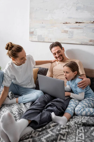 Cheerful parents and shocked kid watching movie on laptop in bedroom — Stockfoto