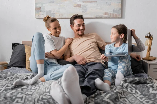 Cheerful parents looking at happy kid holding laptop in bedroom — Stock Photo