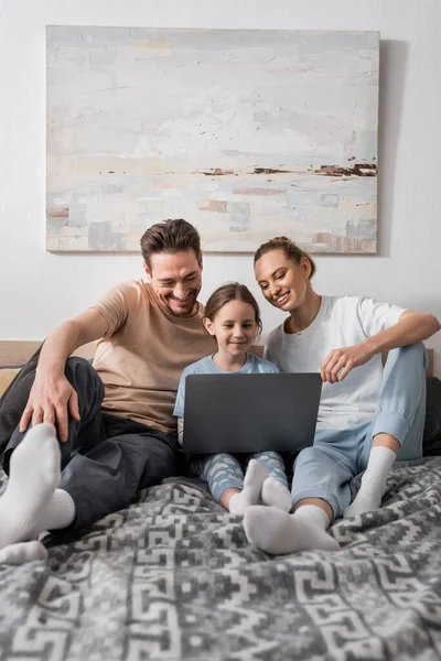 Cheerful parents and happy daughter watching movie on laptop in bedroom — Fotografia de Stock