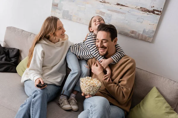 Happy kid hugging bearded father with popcorn near smiling mother — Foto stock