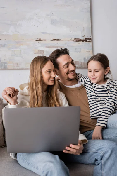 Happy parents holding hands near daughter looking at laptop in living room — Fotografia de Stock