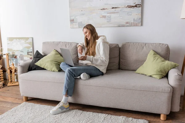 Full length of positive woman in casual clothes having video call on laptop in living room — Photo de stock