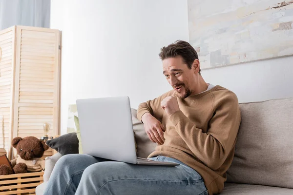 Bearded man watching movie on laptop while sitting on sofa in living room — Foto stock