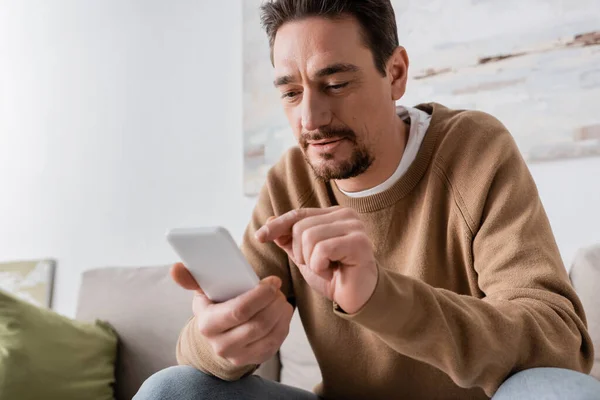 Bearded man in beige jumper using smartphone at home — Stock Photo
