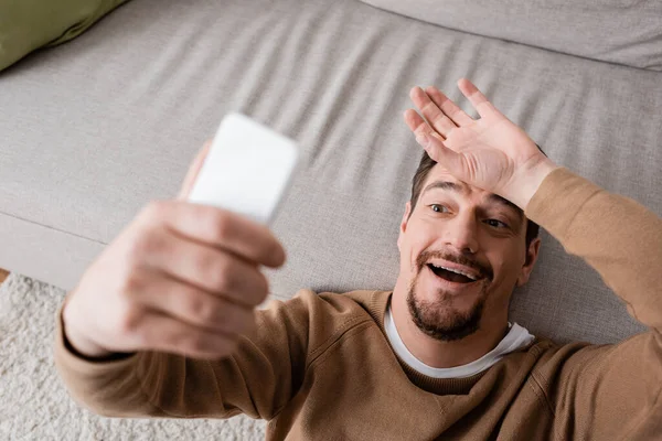 Top view of bearded man in beige jumper holding smartphone and leaning on sofa — Stock Photo