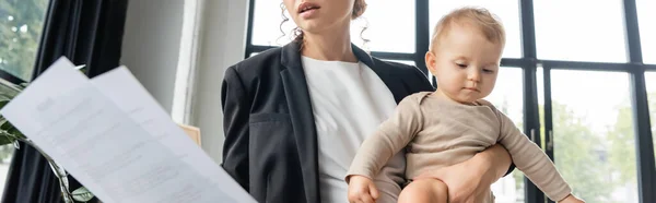 Businesswoman in black blazer holding little daughter and documents in office, banner — Stock Photo