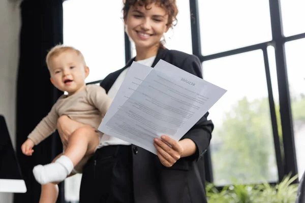 Cheerful businesswoman standing with toddler child and looking at documents in office — Stockfoto