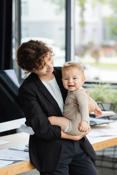 Smiling businesswoman standing with little daughter near workplace in office — Photo de stock
