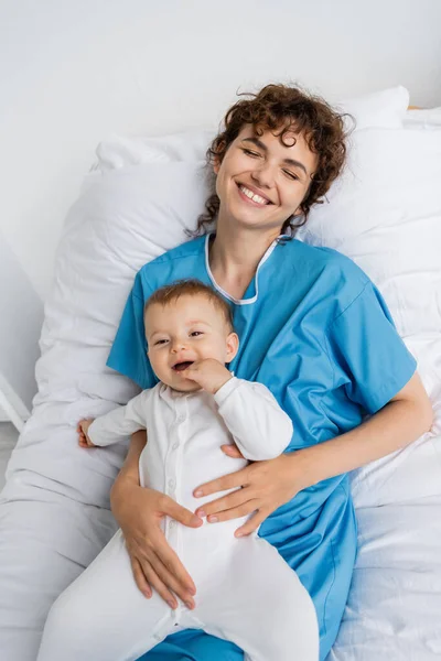 Top view of happy woman holding little daughter and smiling with closed eyes on hospital bed — Stock Photo