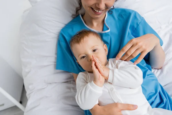 Top view of cheerful woman in patient gown lying on hospital bed with little daughter — Stock Photo