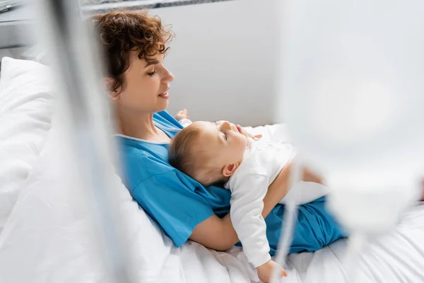 Baby girl with closed eyes sleeping in hands of mother on hospital bed on blurred foreground — Stock Photo