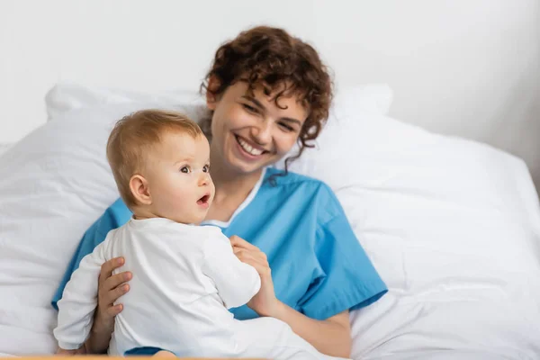 Little baby with open mouth looking away near smiling mother in hospital ward — Stock Photo