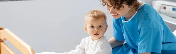 Little girl with open mouth looking at camera near smiling mom in hospital ward, banner — Stock Photo