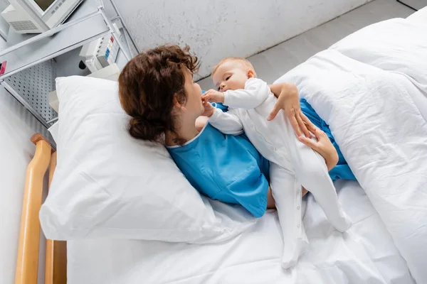 High angle view of baby in romper touching face of mother on bed in clinic — Stock Photo