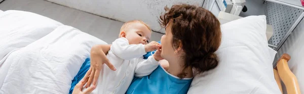 High angle view of toddler girl touching face of mom on bed in hospital ward, banner — Stock Photo