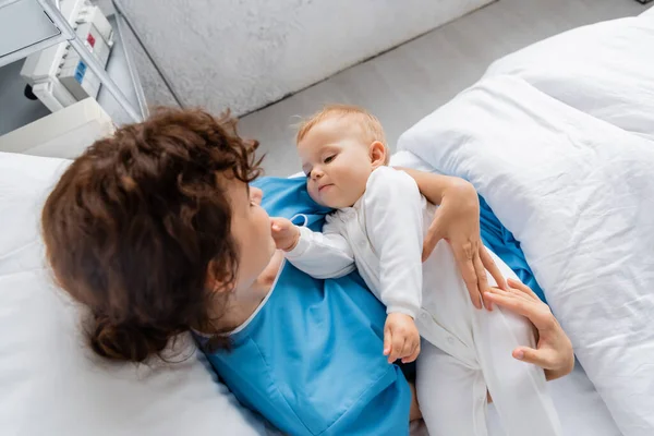 Overhead view of woman in patient gown holding toddler daughter on bed in hospital ward — Stock Photo