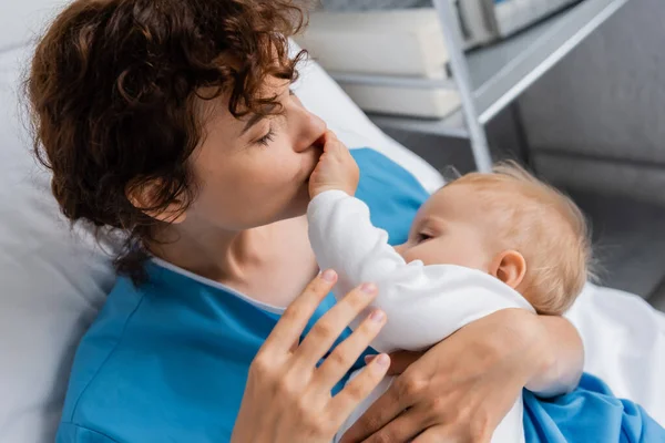 High angle view of woman with closed eyes kissing hand of little daughter in hospital ward — Stock Photo