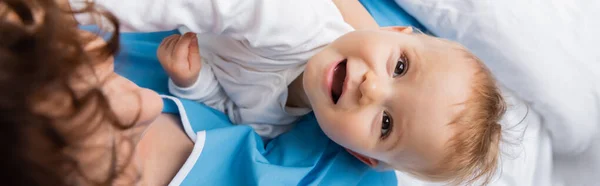 Top view of happy baby girl looking at camera near blurred mother in clinic, banner — Stock Photo