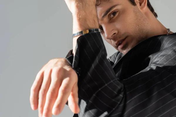 Fashionable man in black blazer and silver bracelet looking at camera on blurred foreground isolated on grey — Stockfoto