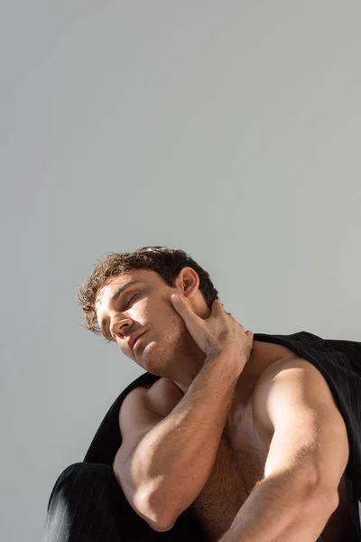 Sexy shirtless man with closed eyes touching neck while posing under black blazer isolated on grey - foto de stock