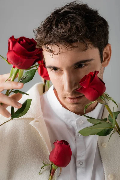 Портрет брюнетки в білій сорочці і куртці біля червоних свіжих троянд ізольовані на сірому — стокове фото