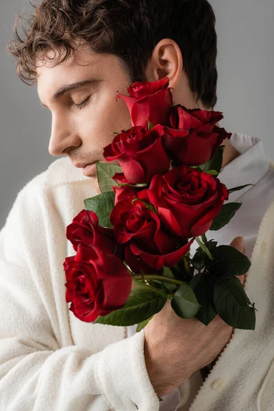 Людина з закритими очима тримає букет червоних свіжих троянд ізольовані на сірому — стокове фото