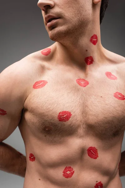 Partial view of sexy shirtless man with red lipstick marks on muscular body isolated on grey - foto de stock